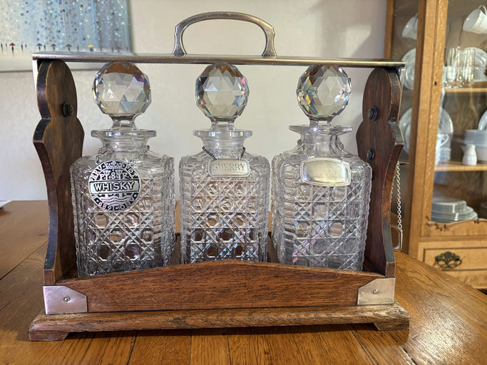 Three crystal decanters labeled "Whisky," "Sherry," and "Gin," elegantly displayed in a wooden holder, set on a wooden table.