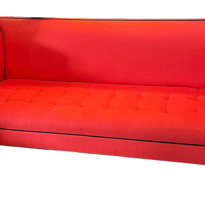 Bright red modern couch with black trim, featuring tufted upholstery. Set in a stylish interior with decorative plants and lamps in the background.