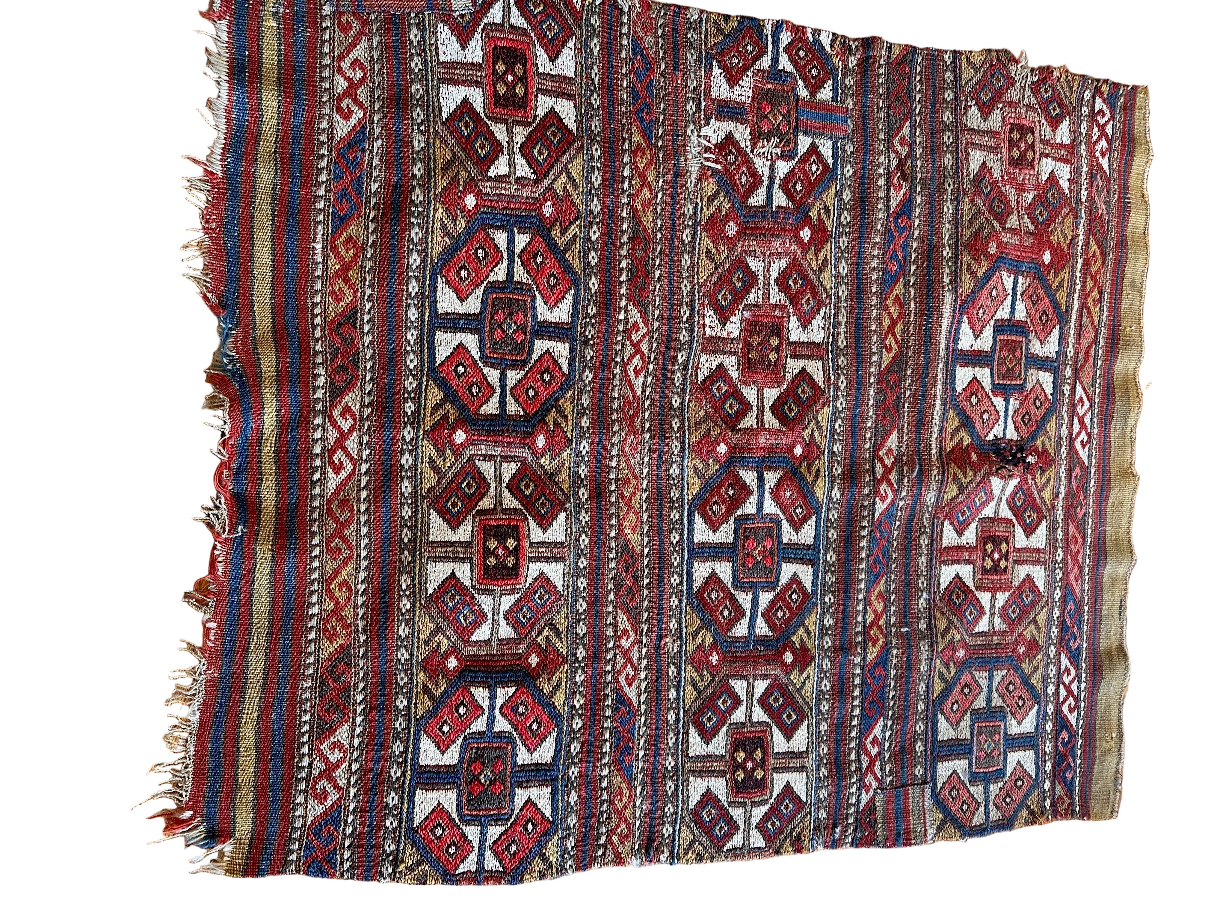 A vibrant, intricately woven textile featuring geometric patterns in red, brown, and cream, displayed against a wooden floor background.