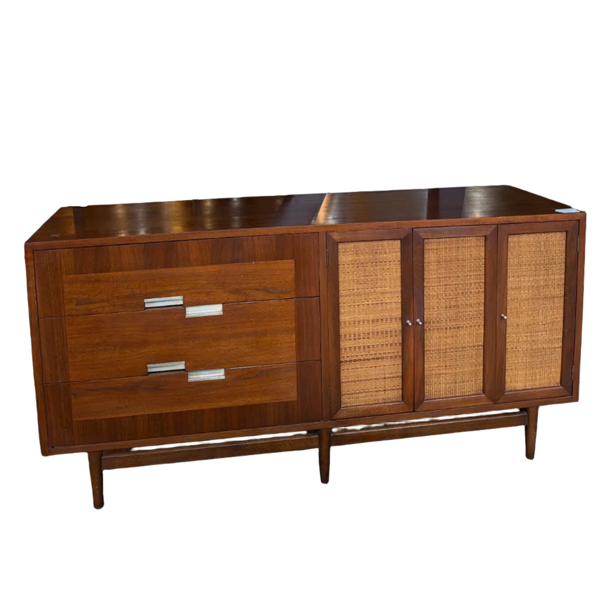 A mid-century modern wooden credenza or sideboard cabinet with two drawers on the left and two cane-embossed doors on the right, photographed in a furniture showroom.