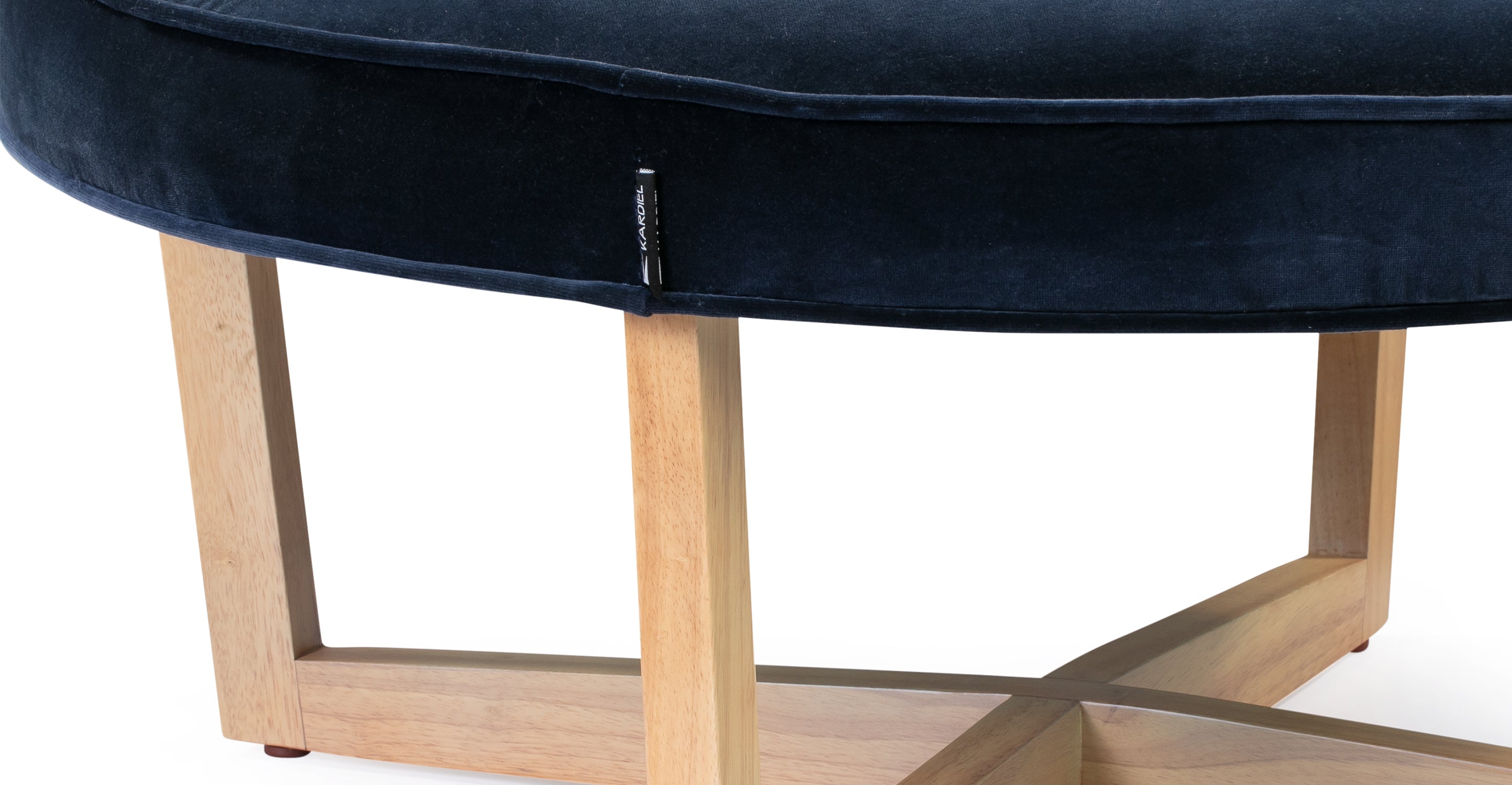 Zoom in on Compass ottoman showing the Kardiel tag and the legs that connect underneath the ottoman making a shape of an X.