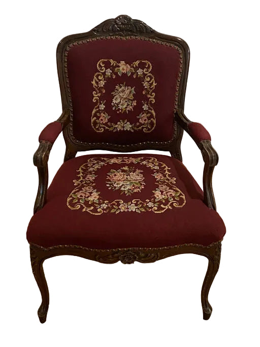 Antique armchair with ornate wooden frame and burgundy upholstery, featuring floral embroidery on the backrest and seat, placed on a wooden floor.
