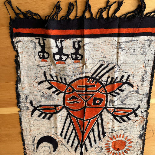 A colorful textile featuring a central red design resembling a sun or mask, surrounded by intricate patterns, with black and orange detailing.