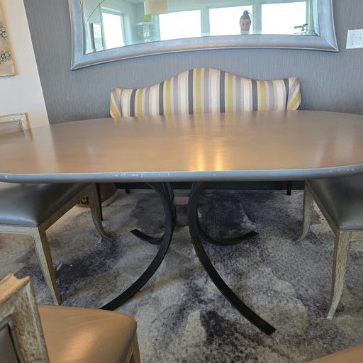 A modern dining area features an elliptical table with a sleek metal base, surrounded by light-colored chairs and a mirrored backdrop.