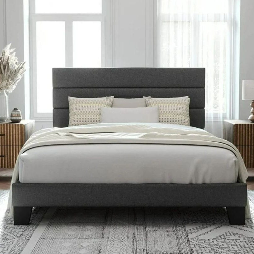 A modern bedroom featuring a gray upholstered bed with two decorative pillows. Light curtains frame the windows, and wooden nightstands add warmth.