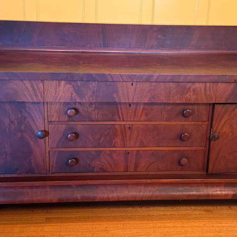 A vintage wooden dresser with a dark cherry finish, featuring four drawers and a storage cabinet, resting on carved lion paw feet.