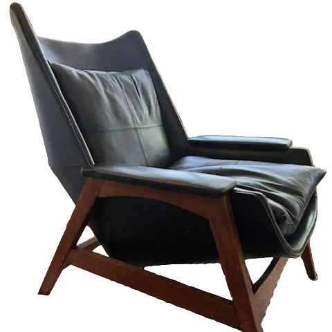 A sleek black leather chair with wooden legs sits beside a window, casting soft light across a striped rug and illuminating the cozy interior.