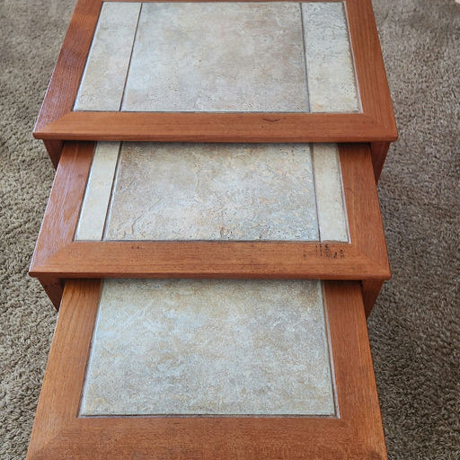 Three nested tables with wooden frames and textured stone-like surfaces, arranged on a carpeted floor, showcasing a simple, modern design.
