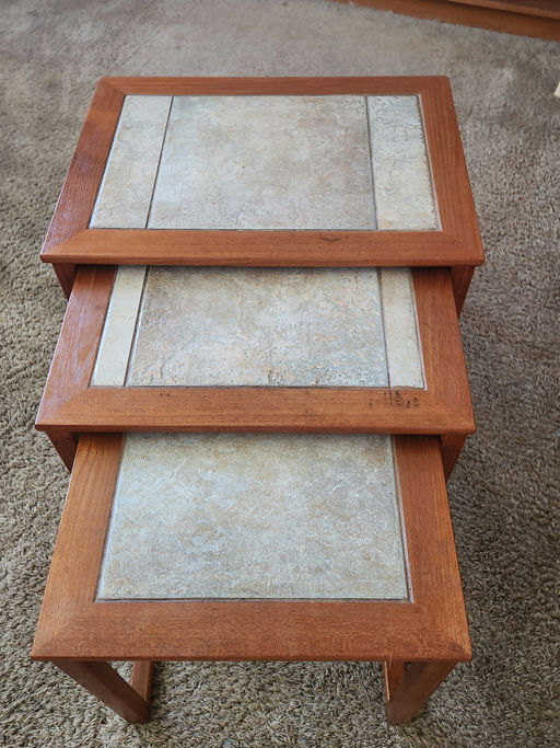 Three nested tables with wooden frames and textured stone-like surfaces, arranged on a carpeted floor, showcasing a simple, modern design.