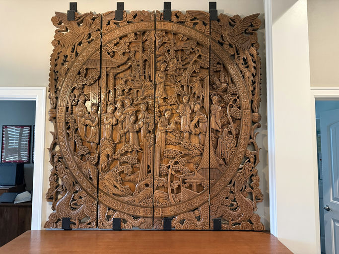Intricate wooden wall art featuring figures, plants, and mythical creatures, elegantly carved with detailed scenes, set against a light background.