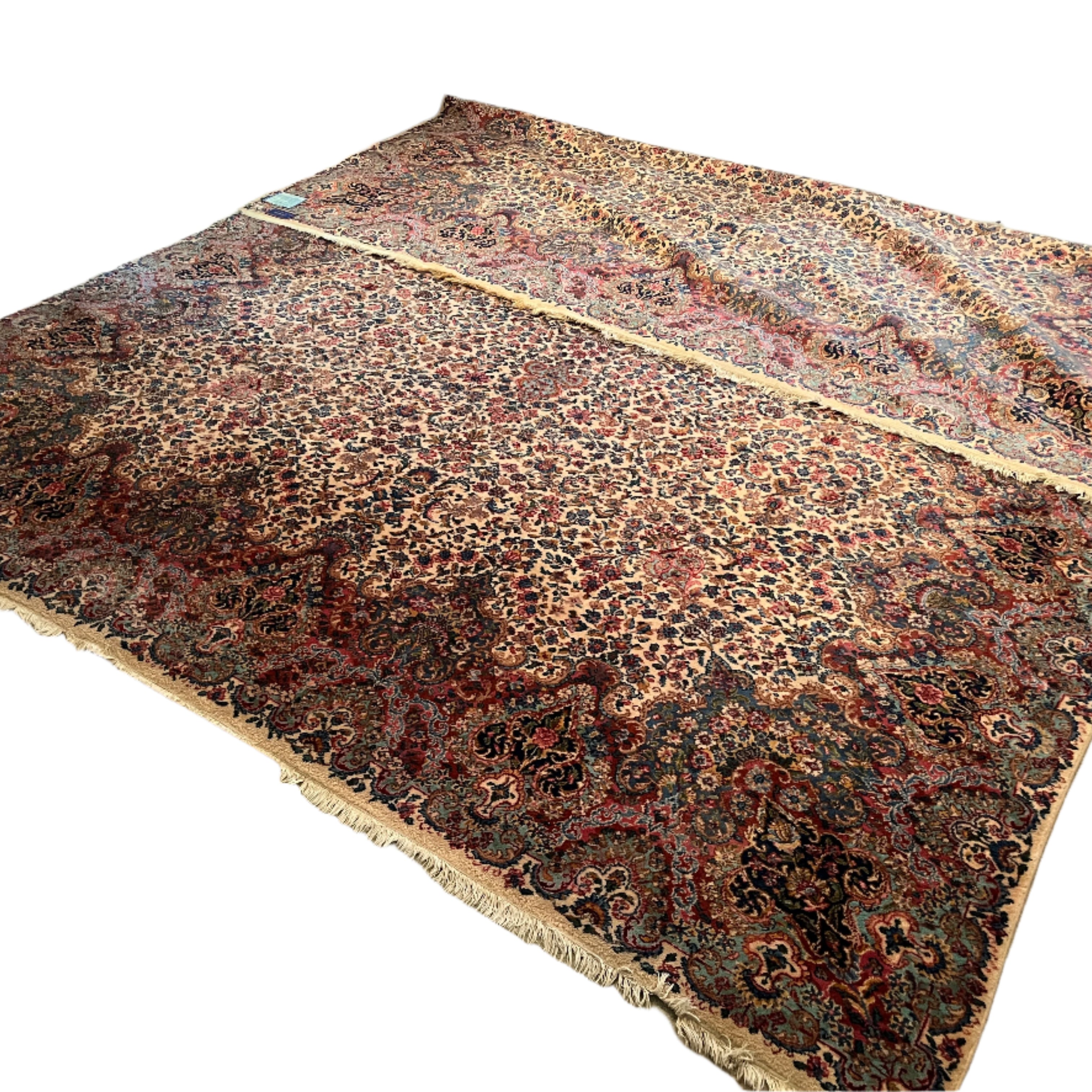 A large, intricately patterned rug covers a carpeted floor. There are two rugs overlapping, featuring rich colors and detailed designs. A sofa is visible.
