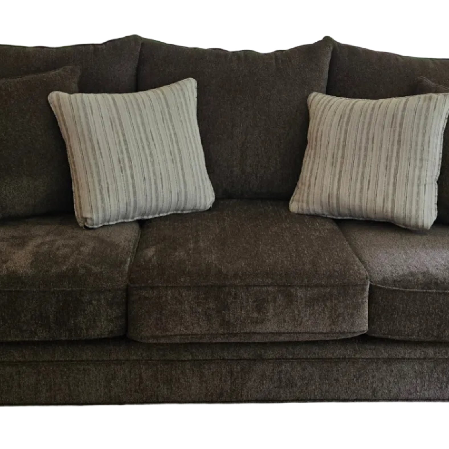 A cozy brown couch with two striped pillows sits in front of glass doors leading to a backyard, surrounded by trees and outdoor furniture.