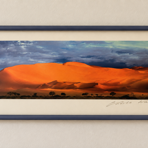 A framed landscape photo depicts vibrant orange sand dunes under a dramatic sky, showcasing the beauty of desert scenery at sunset.