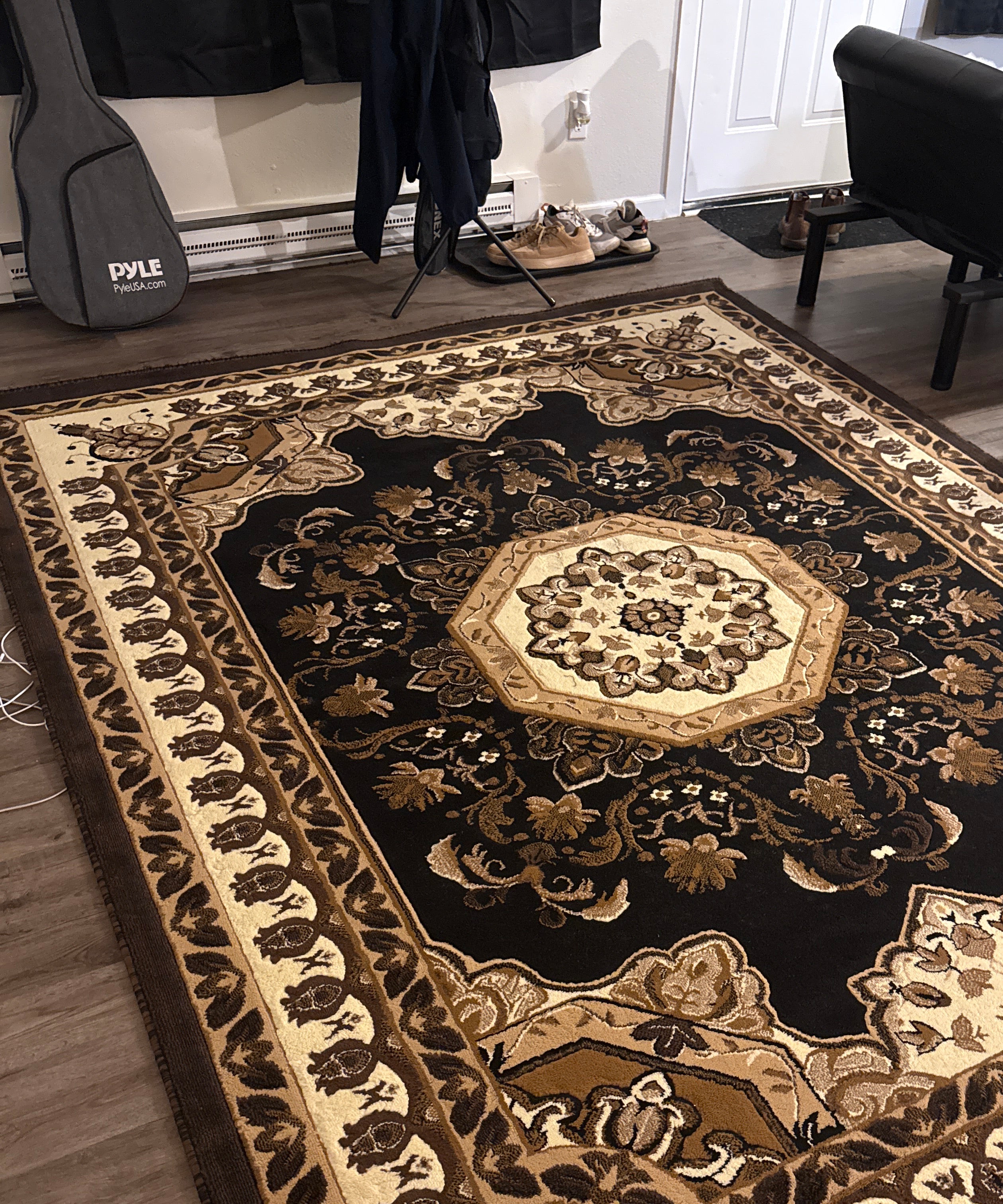 A detailed, ornate area rug with a floral pattern in shades of brown, cream, and gold, placed on a wood floor in a living space.