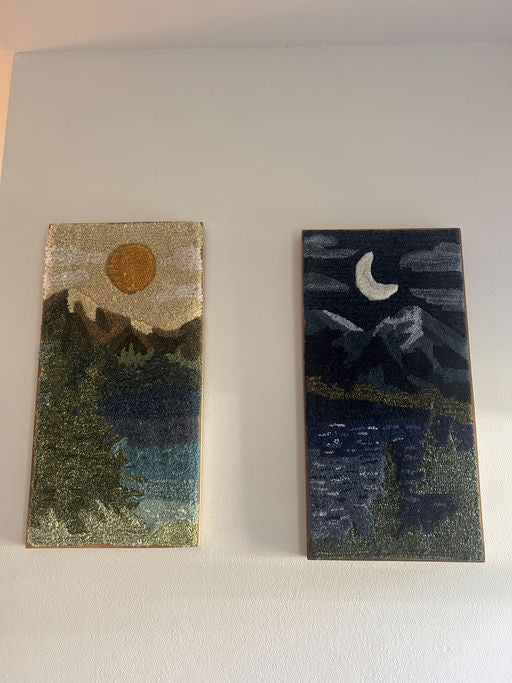 Two framed textile artworks hang on a wall: one depicts a sunny landscape, while the other features a moonlit mountain scene.