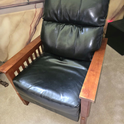 A comfortable black leather recliner with plush cushioning and wooden armrests, set against a softly colored, mural-painted wall.
