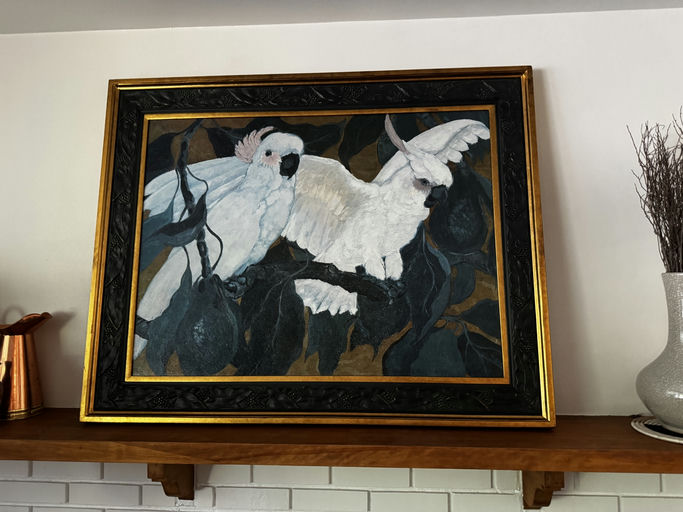 A colorful painting of two white cockatoos perched on branches, surrounded by dark green leaves, framed in an ornate black and gold frame.