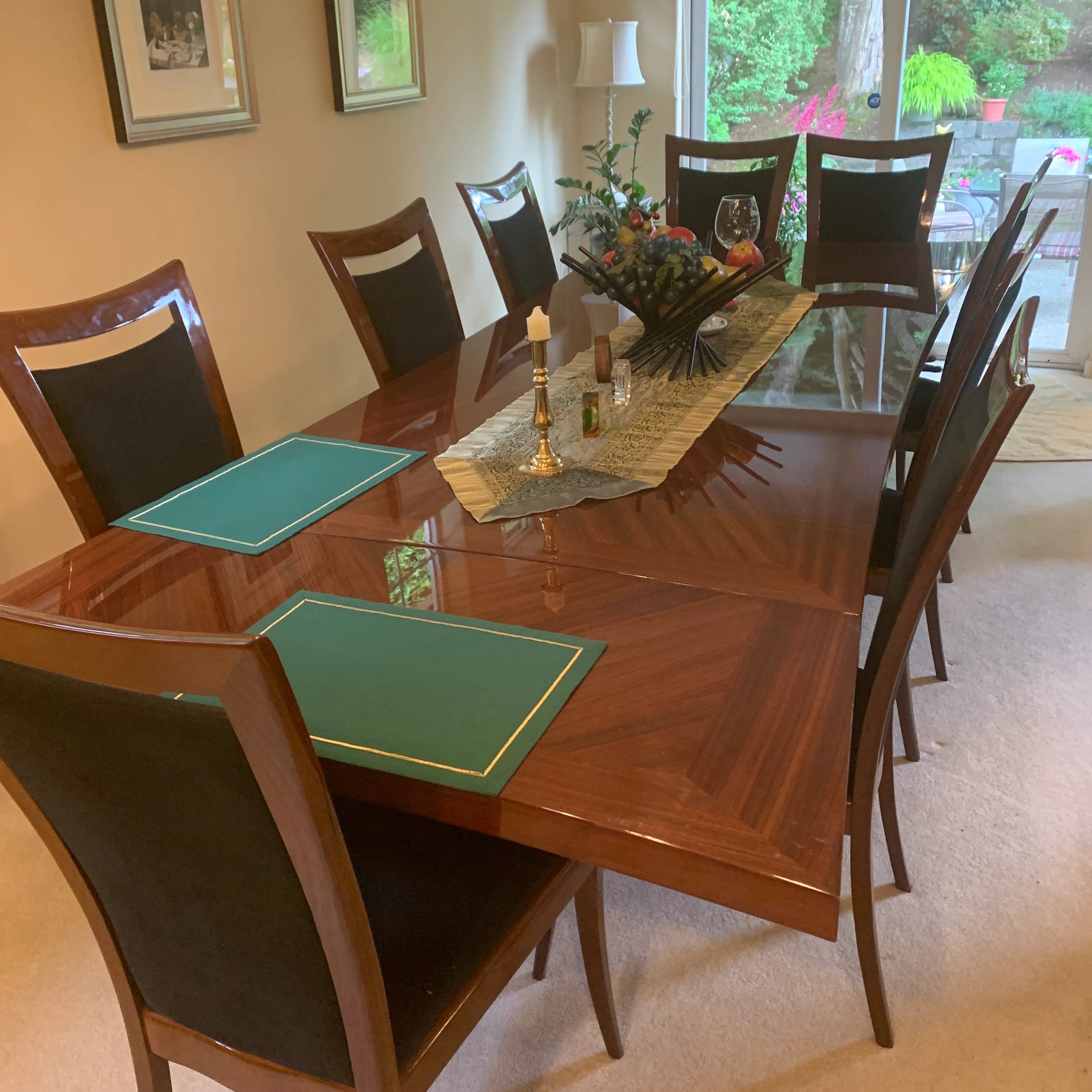 A dining room table set with eight chairs, green placemats, and a decorative centerpiece. Natural light filters through windows.