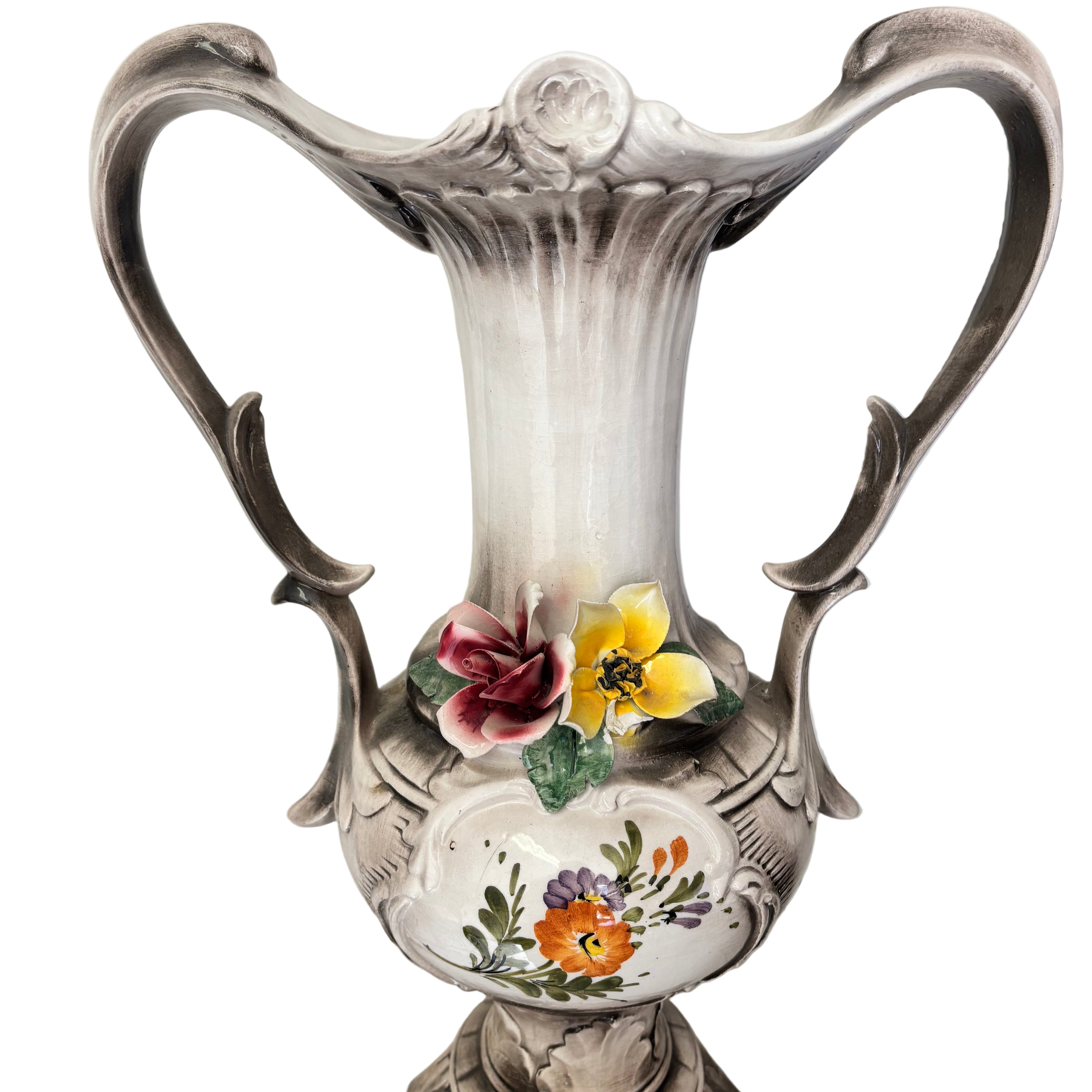 Ceramic vase with ornate design, featuring floral decorations in pink, yellow, and orange. It stands on a decorative base against a tiled surface.
