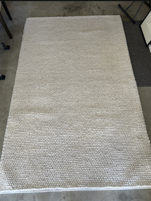 A textured, light-colored area rug with a bubble-like pattern, lying on a concrete floor, adds warmth and style to the space.