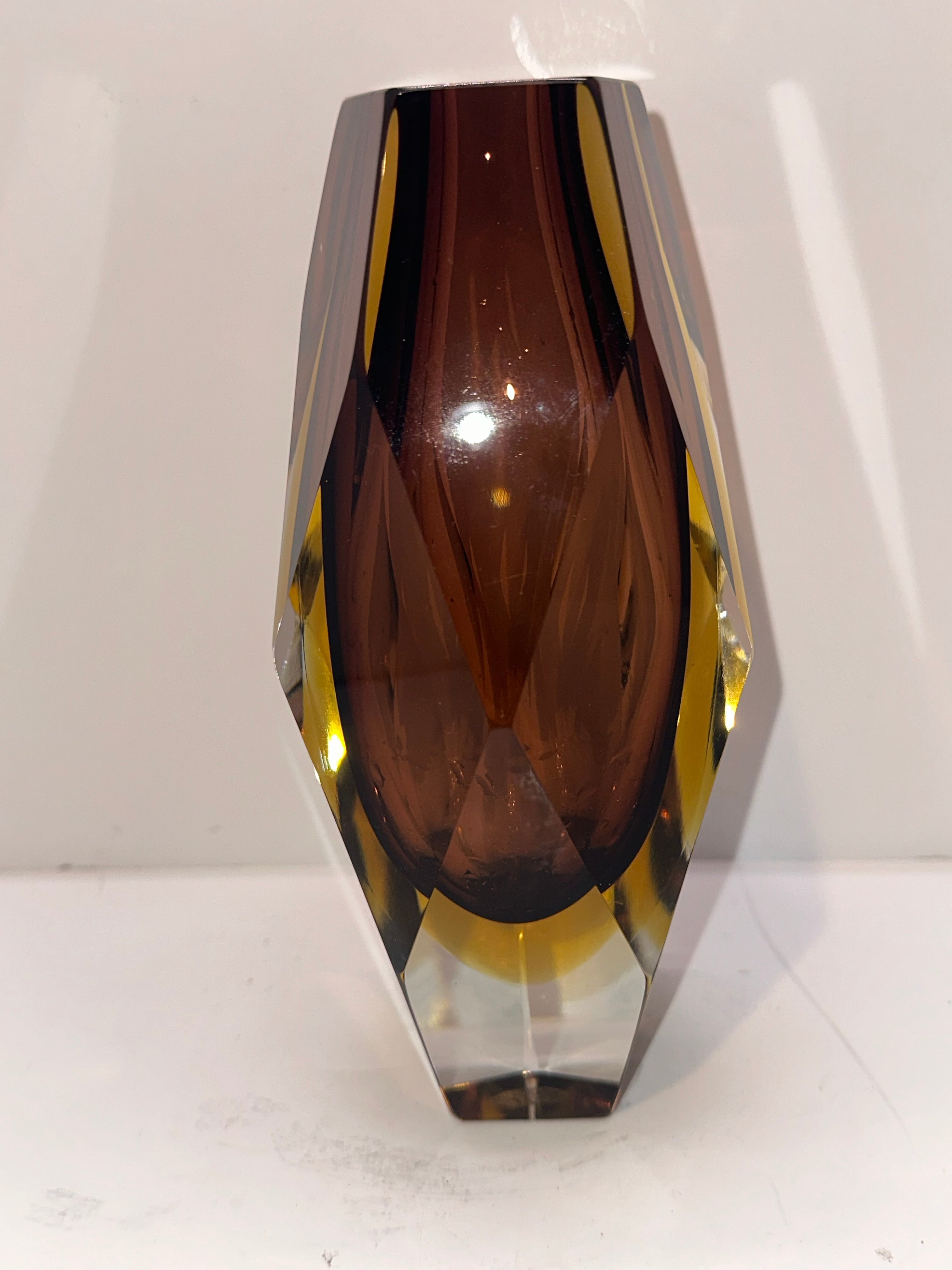 A decorative glass vase featuring a geometric design with rich amber and brown hues, capturing light and enhancing its elegant appearance.