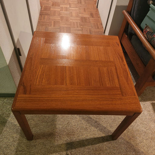A square wooden coffee table with a glossy finish, featuring a geometric pattern on the surface, set in a room with patterned flooring.