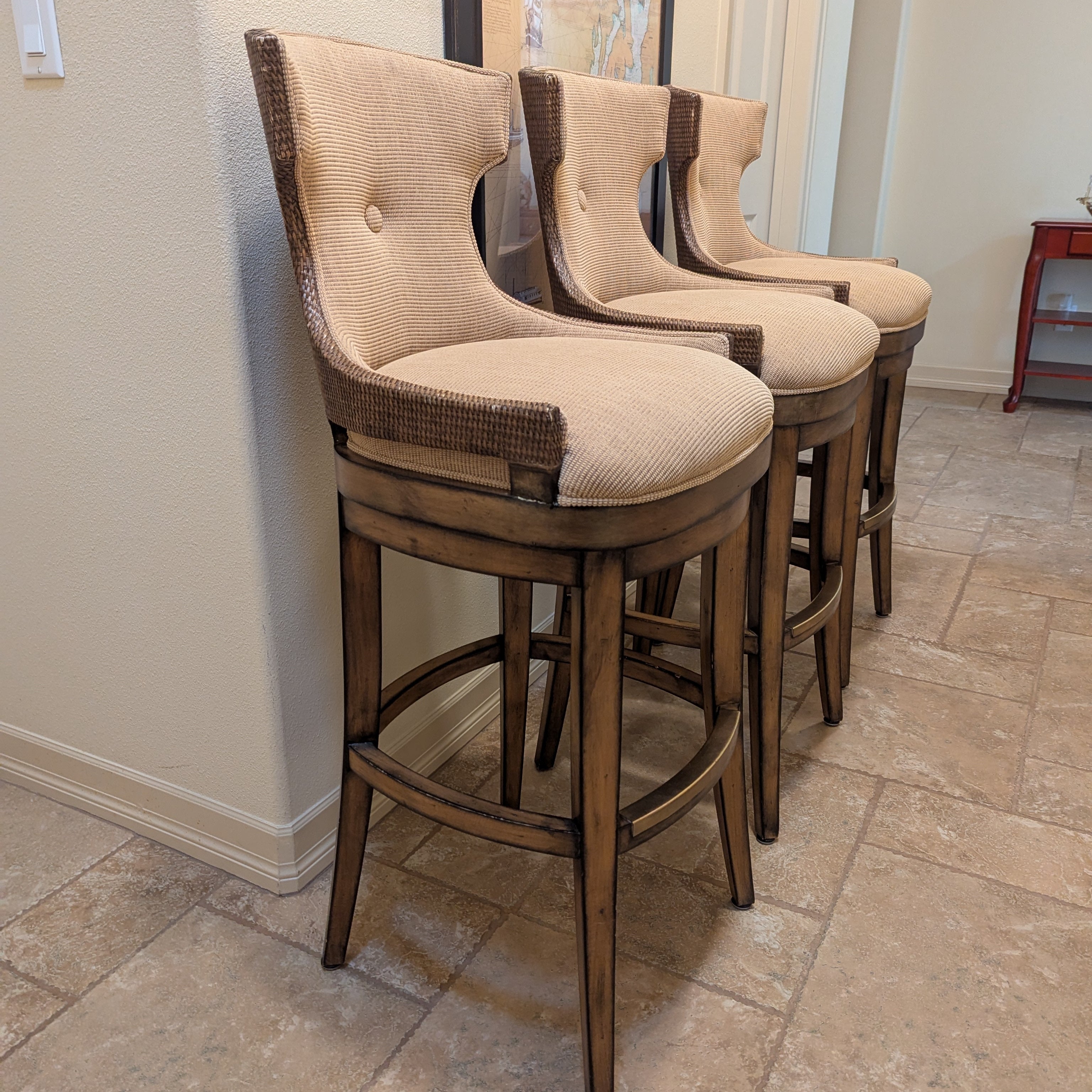 Three stylish barstools with beige cushioned seats and wooden legs, lined against a light-colored wall, complementing a modern interior space.