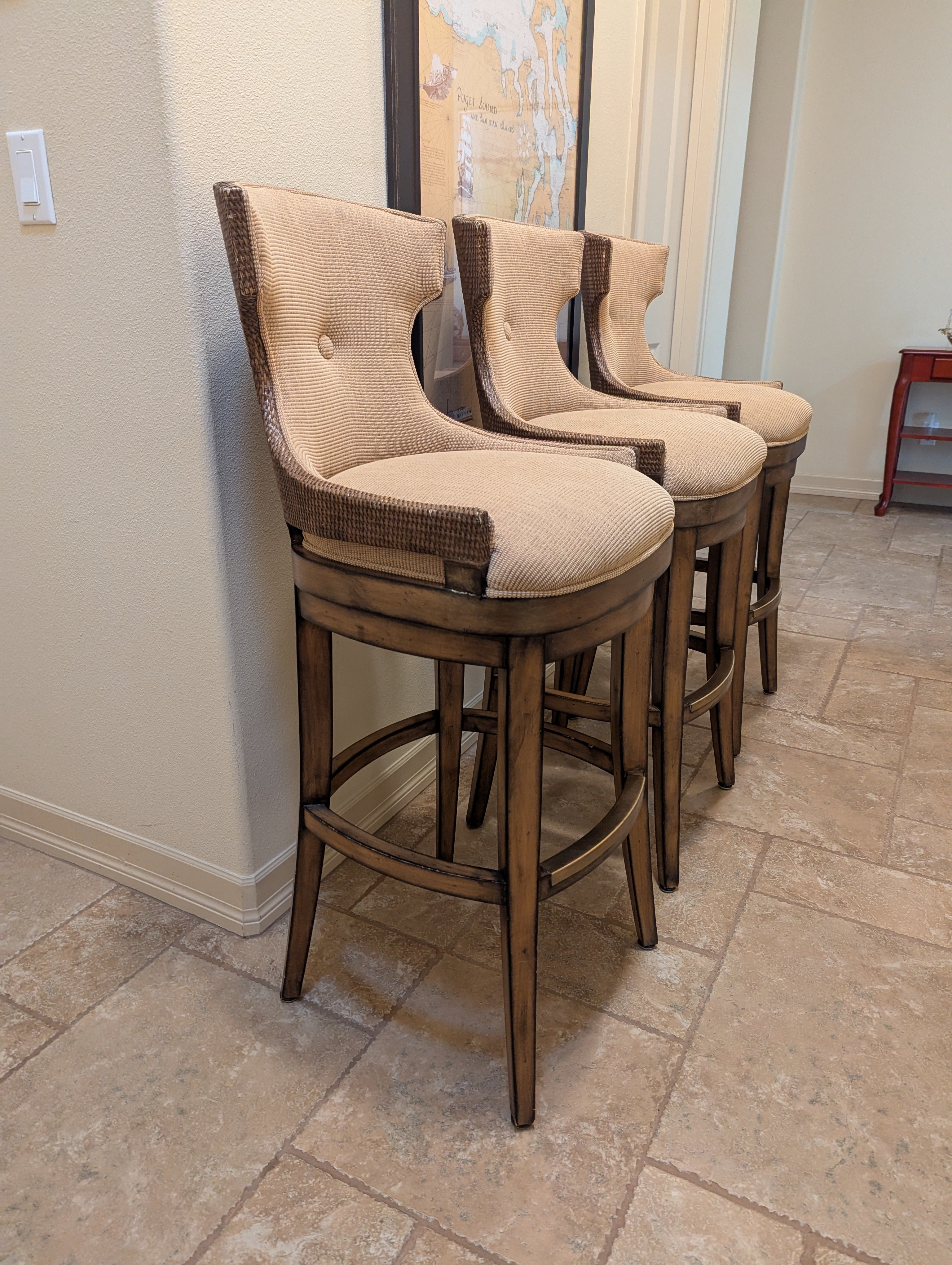 Three stylish barstools with beige cushioned seats and wooden legs, lined against a light-colored wall, complementing a modern interior space.