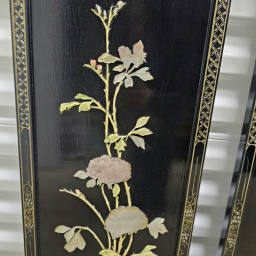 Intricate floral design on a black background, featuring soft-colored blossoms, leaves, and delicate detailing, displayed on an ornate panel.