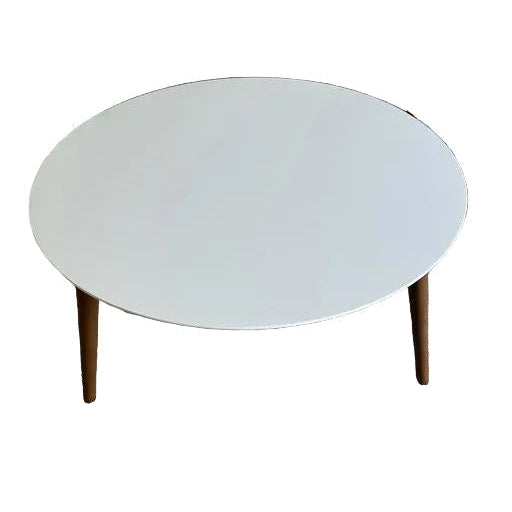 A modern round coffee table with a white top and wooden legs, placed on beige carpet, with a staircase visible in the background.
