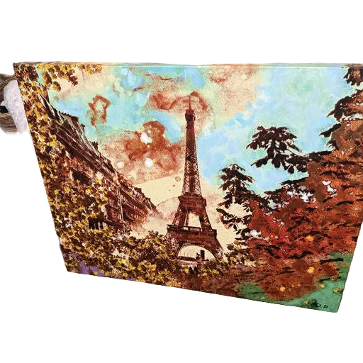 An artistic canvas featuring the Eiffel Tower, surrounded by vibrant autumn foliage and a colorful sky, set against a brick backdrop.