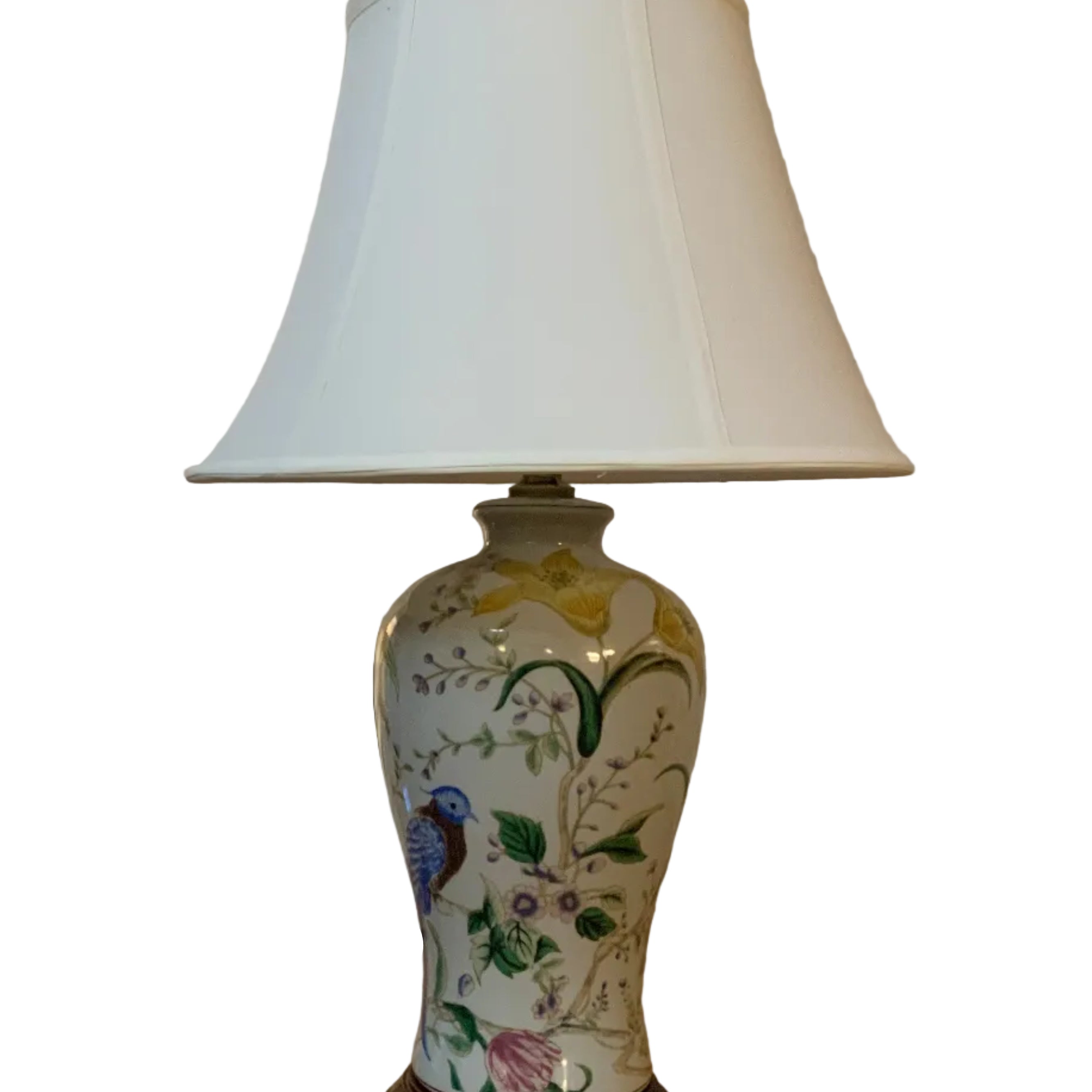 A decorative table lamp with a white lampshade and a floral ceramic base featuring a colorful bird, positioned on a wooden table.
