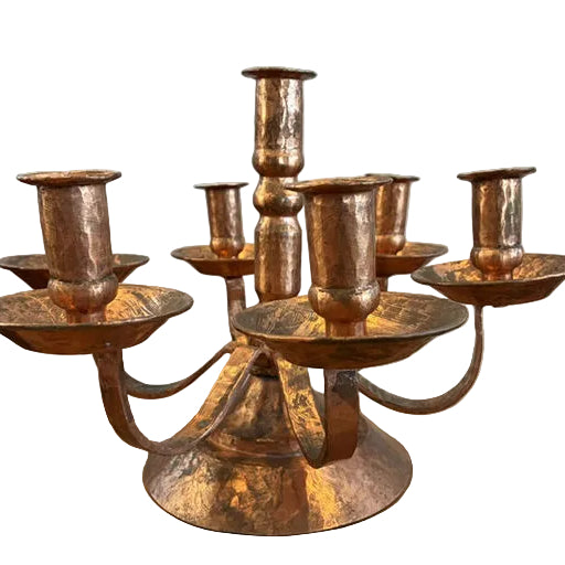 A vintage copper candlestick holder with six candle holders, featuring a textured finish and a rounded base, set on a wooden surface.