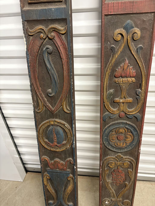 Two ornate wooden panels with colorful carvings, featuring various designs like flames, flowers, and shapes, displayed against a storage background.