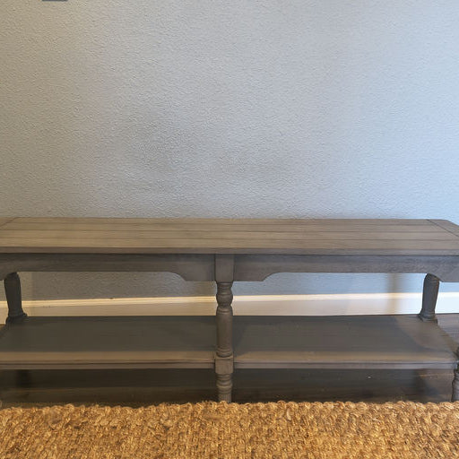 A gray wooden console table with two shelves, featuring turned legs and a smooth top, positioned against a light blue wall.