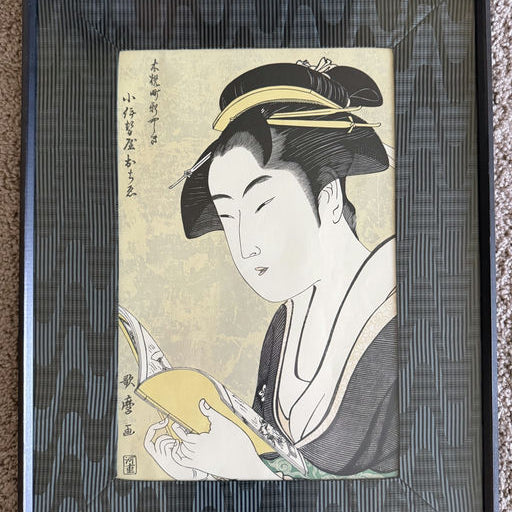 A framed traditional Japanese woodblock print features a woman reading a book, showcasing intricate patterns and vibrant colors in her attire.