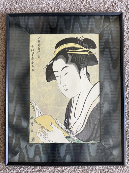 A framed traditional Japanese woodblock print features a woman reading a book, showcasing intricate patterns and vibrant colors in her attire.