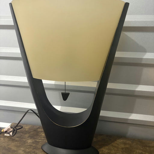 A modern black table lamp with a semi-circular frosted shade, featuring a pull chain switch and set against a textured grey background.