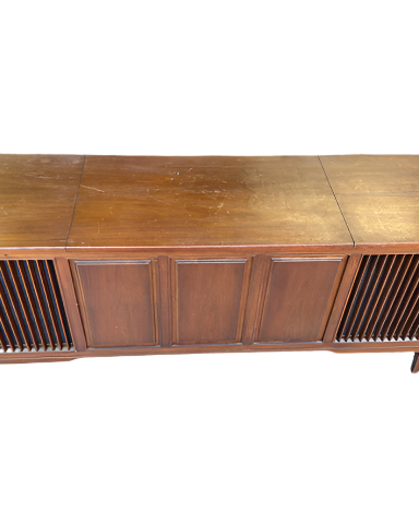 A vintage wooden credenza with slatted doors, situated on a concrete floor. Surrounded by other wooden furniture pieces in a workshop setting.