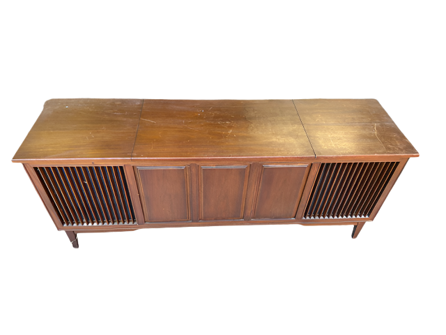 A vintage wooden credenza with slatted doors, situated on a concrete floor. Surrounded by other wooden furniture pieces in a workshop setting.