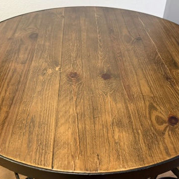 A round wooden table with a smooth, polished surface, featuring a rich grain pattern and a dark finish. Minimalist metal legs are visible.