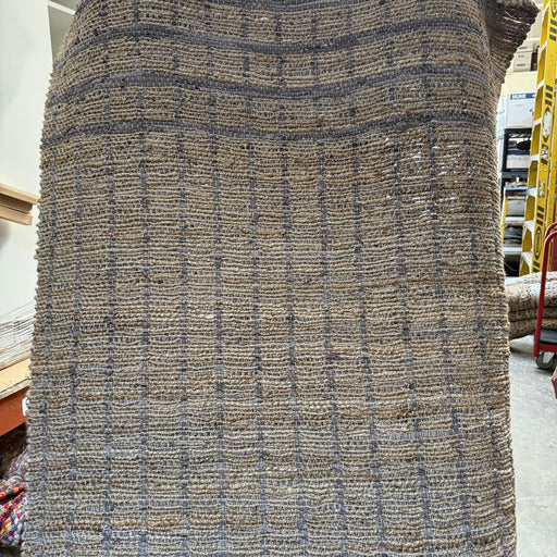 A textured woven rug displayed vertically, featuring a grid pattern in shades of brown and gray, highlighting its natural fibers and craftsmanship.