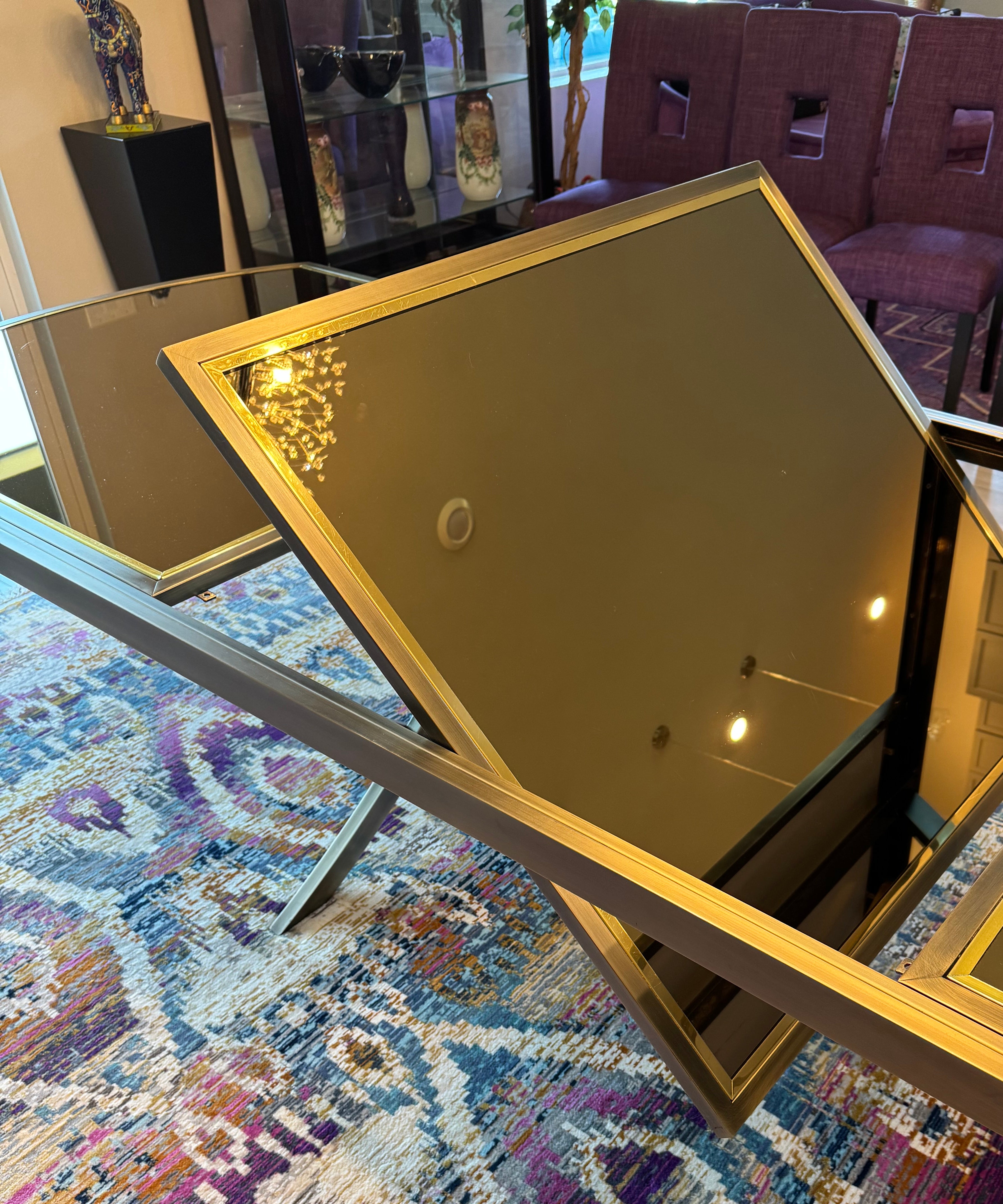 A sleek, modern coffee table with glass surfaces sits on a colorful patterned rug. Background features purple chairs and decorative items.