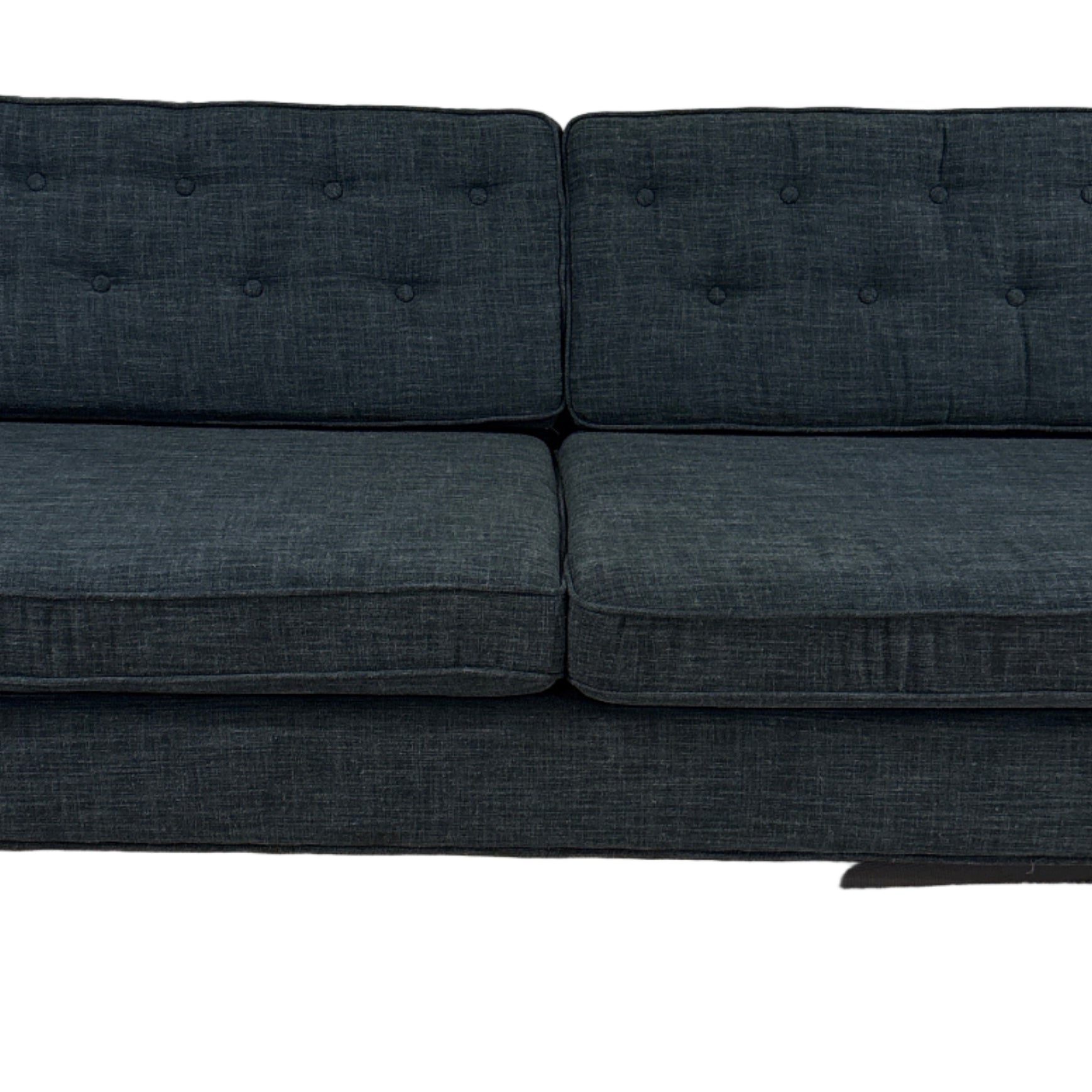 A modern, dark blue fabric sofa with button-tufted back cushions, two seats, and wooden legs, positioned on a light carpet against a plain wall.