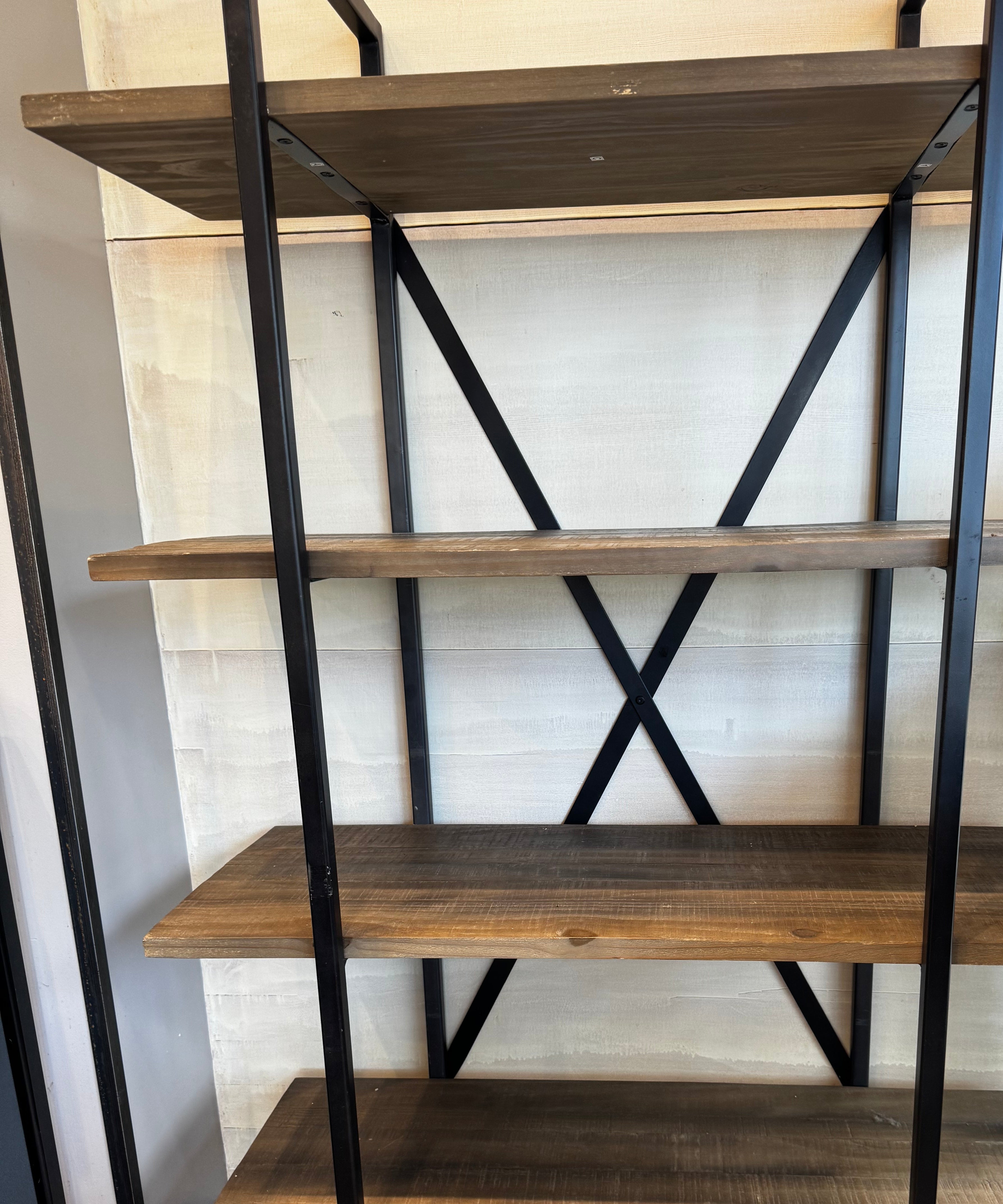 A five-shelf industrial-style shelving unit made of wooden planks and black metal frame. The background features a light-colored wall.