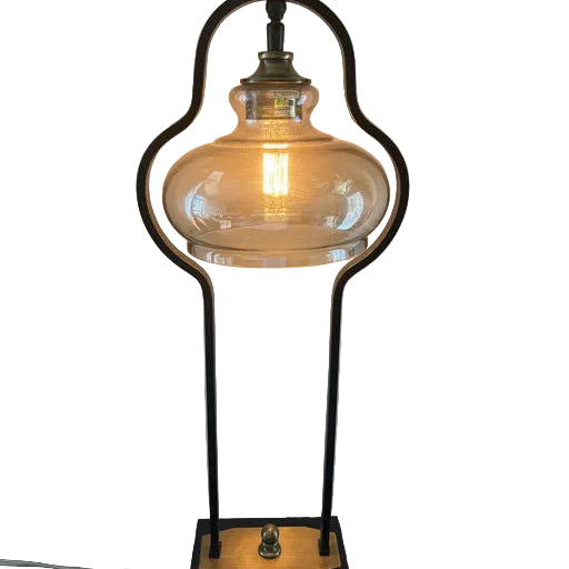 A stylish table lamp with a glass shade and a vintage bulb, set on a black base with a gold accent, providing warm, ambient light.