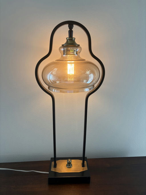 A stylish table lamp with a glass shade and a vintage bulb, set on a black base with a gold accent, providing warm, ambient light.