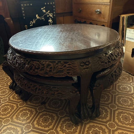 A carved wooden round table sits in a room with vintage decor, featuring intricate designs and a glossy surface, with patterned flooring visible.