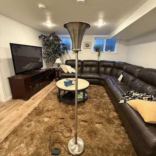 A modern living room featuring a silver floor lamp, a brown leather sectional sofa, a round coffee table, and a patterned carpet.