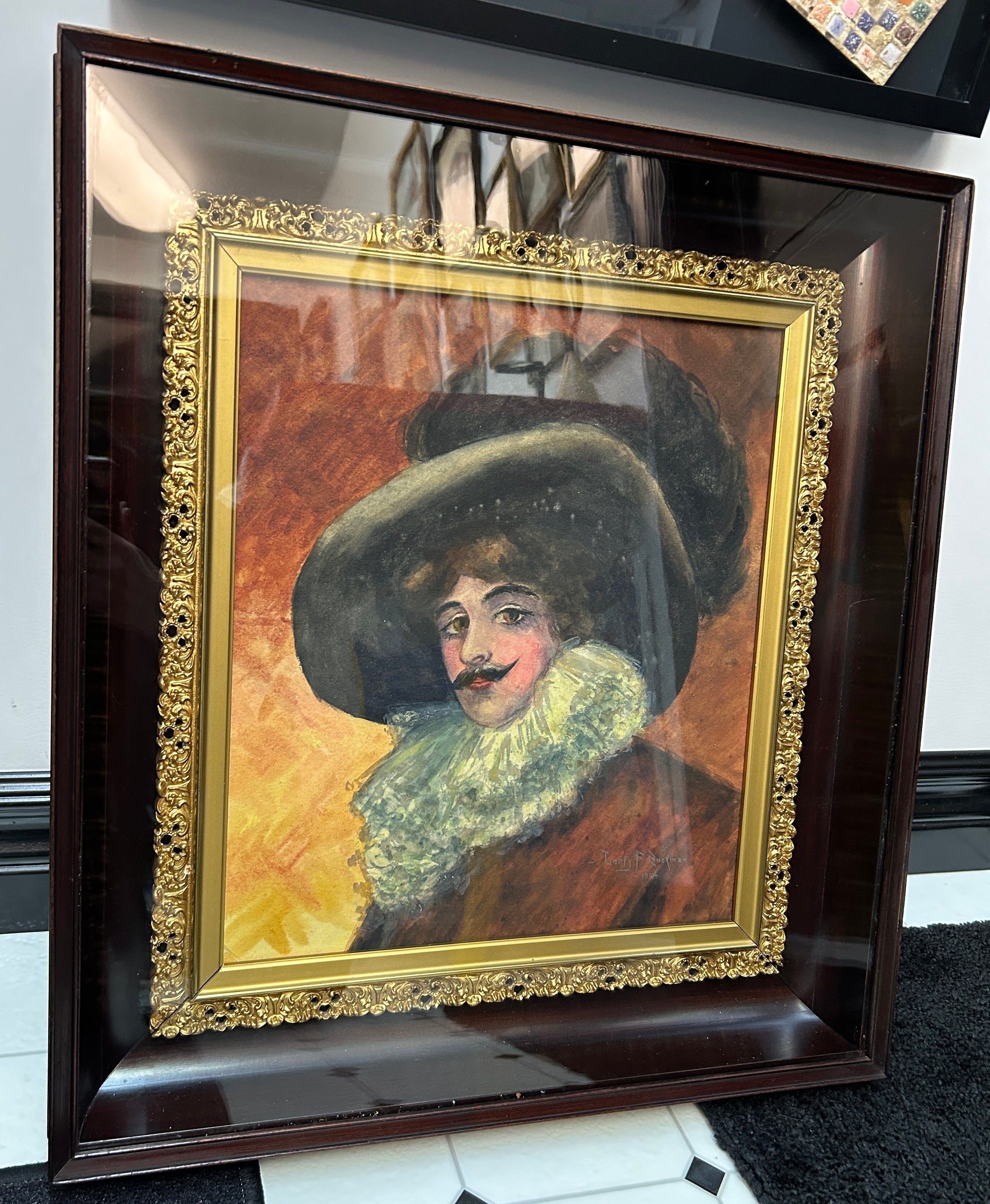 A framed portrait featuring a man with a large hat and ruffled collar, painted in warm tones, displayed against a patterned background.